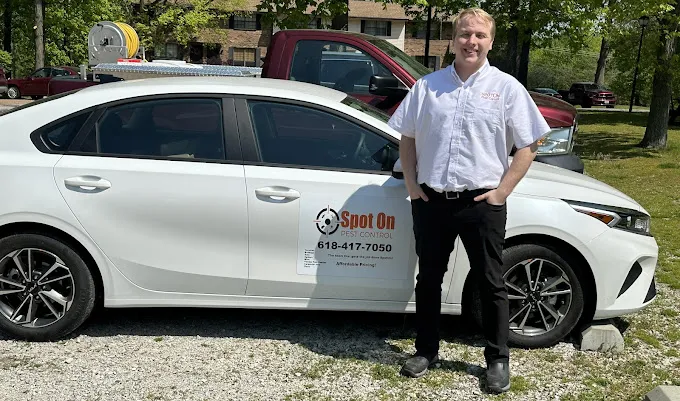 A member of the Spot On team standing beside the company car, which is lettered with the Spot On logo and phone number.